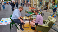 Zwei Männer spielen Schach auf den Sommerstraßen. Hinter ihnen sind viele Menschen zu sehen.