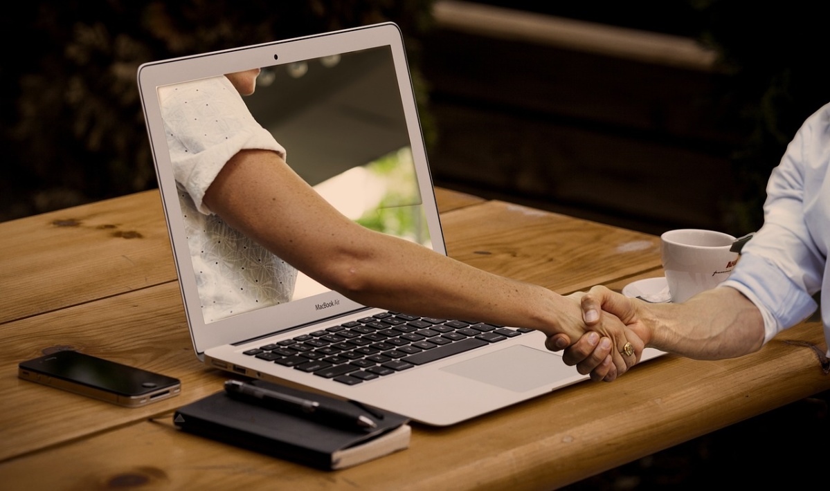 Auf dem Foto ist ein PC zu sehen, aus dem ein Arm kommt, der der Person vor dem PC die Hand gibt