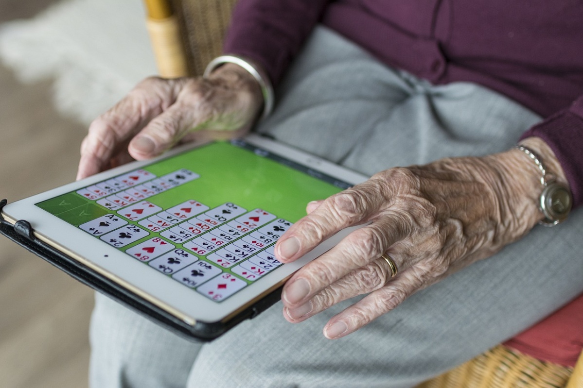 auf dem Foto befindet sich ein Tablet, gehalten von den Hännden einer alten Frau, auf dem Solitär gespielt wird.