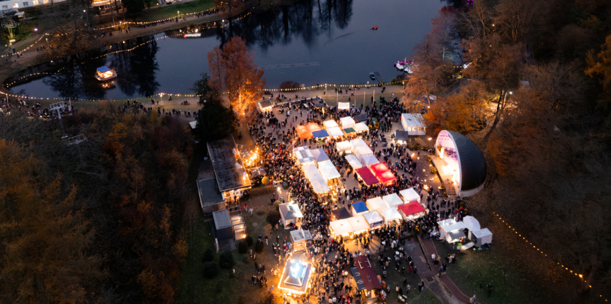 Blick von oben auf den Deutschmühlenweiher mit beleuchteten Ständen und der Seebühne