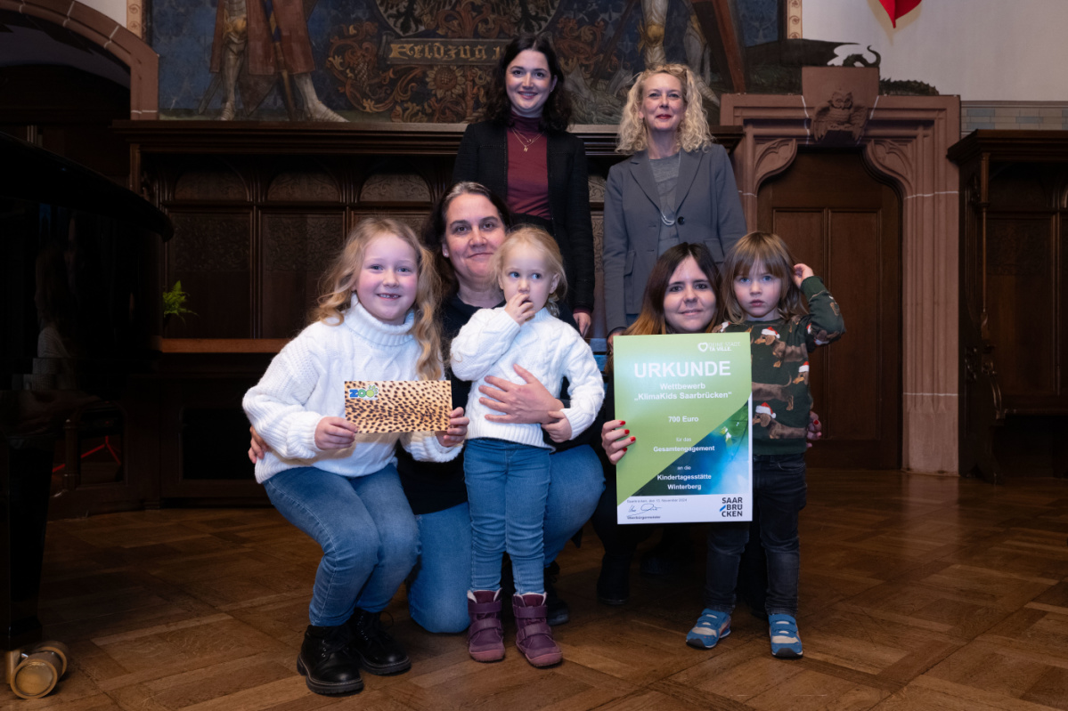  Preisübergabe an die Kita Winterberg. Zu sehen sind drei Schüler welche die Urkunde halten und eine Betreuerin der Kita, sowie zwei Jurymitglieder.