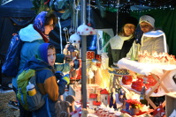 Illumininierter Verkaugsstand mit Verkäuferinnen und Besucherin mit Kind