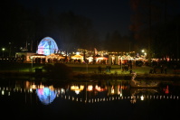 Blick auf den Weihnachtsgarten bei Nacht, im Vordergrund der Weiher, in dem sich die Lichter des Weihnachtsgartens spiegeln