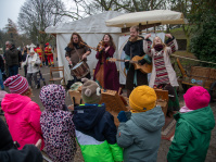 Eine Musikgruppe aus vier Personen mit Trommel, Gitarre und Tambourin spielen einer Gruppe von Kindern etwas vor