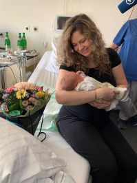 Mutter mit hält Baby auf dem Armt, im Zimmer eines Krankenhauses, links im Bild Blumen 