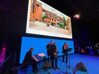 Eine Band mit vier Musikern auf einer Bühne, im Hintergrund ein Foto des Antiquariats in der Türkenstraße, Saarbrücken