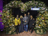 Drei Frauen und zwei Männer vor einem großen herzförmigen Blumenarrangement 