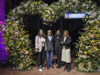 Drei lächelnde Menschen vor einem großen herzförmigen Blumenarrangement 