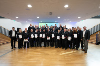 Eine Gruppe Personen in Uniform steht in Reihen und hält weiße Mappen fest